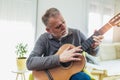 Mature man in casual clothes is smiling while playing guitar at home Royalty Free Stock Photo