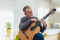 Mature man in casual clothes is smiling while playing guitar at home Royalty Free Stock Photo