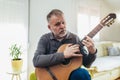 Mature man in casual clothes is smiling while playing guitar at home Royalty Free Stock Photo