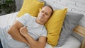 Handsome, mature man lounging in a cozy, comfortable bed, lost in thought, arms crossed in a serious, relaxed morning at home Royalty Free Stock Photo