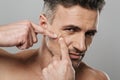 Handsome mature man naked take care of his skin squeezes out a pimple.