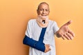 Handsome mature senior man wearing cervical collar and arm on sling smiling cheerful offering palm hand giving assistance and Royalty Free Stock Photo