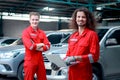 Handsome mechanic men in red uniform holding laptop computer standing at vehicle garage, auto mechanic technician teamwork working Royalty Free Stock Photo