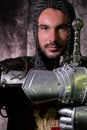 Portrait of handsome medieval knight in suit of armour with beard and blue eyes looking at camera and holding sword Royalty Free Stock Photo