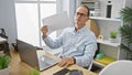 Handsome middle age business worker suffers in office heat, fanning himself with work documents Royalty Free Stock Photo