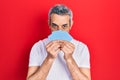 Handsome middle age man with grey hair covering face with cards relaxed with serious expression on face