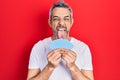 Handsome middle age man with grey hair covering face with cards sticking tongue out happy with funny expression