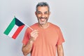 Handsome middle age man with grey hair holding kuwait flag looking positive and happy standing and smiling with a confident smile