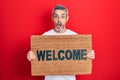 Handsome middle age man with grey hair holding welcome doormat afraid and shocked with surprise and amazed expression, fear and Royalty Free Stock Photo