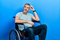 Handsome middle age man with grey hair sitting on wheelchair confuse and wondering about question Royalty Free Stock Photo