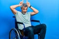 Handsome middle age man with grey hair sitting on wheelchair doing funny gesture with finger over head as bull horns