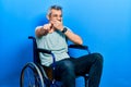 Handsome middle age man with grey hair sitting on wheelchair laughing at you, pointing finger to the camera with hand over mouth, Royalty Free Stock Photo