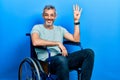 Handsome middle age man with grey hair sitting on wheelchair showing and pointing up with fingers number four while smiling