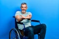 Handsome middle age man with grey hair sitting on wheelchair smiling with hands palms together receiving or giving gesture Royalty Free Stock Photo