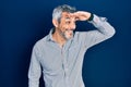 Handsome middle age man with grey hair wearing business shirt very happy and smiling looking far away with hand over head Royalty Free Stock Photo