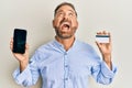 Handsome middle age man holding smartphone and credit card angry and mad screaming frustrated and furious, shouting with anger Royalty Free Stock Photo