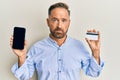 Handsome middle age man holding smartphone and credit card depressed and worry for distress, crying angry and afraid Royalty Free Stock Photo