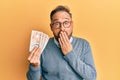 Handsome middle age man holding 10 united kingdom pounds banknotes covering mouth with hand, shocked and afraid for mistake