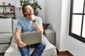 Handsome middle age man using computer laptop on the sofa with hand on chin thinking about question, pensive expression Royalty Free Stock Photo