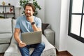 Handsome middle age man using computer laptop on the sofa pointing to the eye watching you gesture, suspicious expression Royalty Free Stock Photo