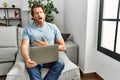 Handsome middle age man using computer laptop on the sofa in shock face, looking skeptical and sarcastic, surprised with open Royalty Free Stock Photo