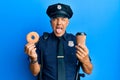 Handsome middle age mature police man eating donut and drinking coffee sticking tongue out happy with funny expression Royalty Free Stock Photo