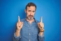 Handsome middle age senior man with grey hair over isolated blue background Pointing up looking sad and upset, indicating Royalty Free Stock Photo