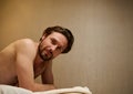 Handsome middle aged Caucasian man lying on a massage table, smiles looking at camera, getting ready to receive professional body Royalty Free Stock Photo