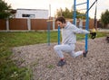 Handsome middle aged Caucasian man working out on a sports track, doing lunges while using fitness suspension straps