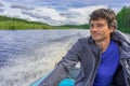 Handsome middle-aged man sitting at boat stern and floating along northern river on beautiful landscape background in summer day.