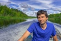 Handsome middle-aged man sitting at boat stern and floating along northern river on beautiful landscape background in summer day.