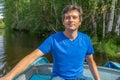 Handsome middle-aged man sitting at boat stern and floating along northern river on beautiful landscape background in summer sunny