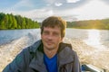 Handsome middle-aged man sitting at boat stern and floating along northern river on beautiful landscape background at sunset. Royalty Free Stock Photo