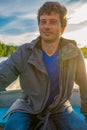 Handsome middle-aged man sitting at boat stern and floating along northern river on beautiful landscape background at sunset. Royalty Free Stock Photo