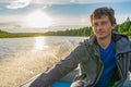 Handsome middle-aged man sitting at boat stern and floating along northern river on beautiful landscape background at sunset. Royalty Free Stock Photo