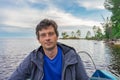 Handsome middle-aged man sitting at boat stern and floating along northern river on beautiful landscape background at sunset. Royalty Free Stock Photo