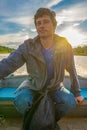 Handsome middle-aged man sitting at boat stern and floating along northern river on beautiful landscape background at sunset. Royalty Free Stock Photo