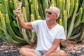 Handsome middle-aged man takes a selfie in front of a large cactus in an exotic seaside resort