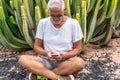 Handsome middle aged man using smartphone in front of a large cactus in an exotic seaside resort