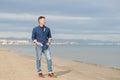 Handsome middle-aged man walking at the beach. Attractive happy smiling mid adult male model posing at seaside in blue jeans, t- Royalty Free Stock Photo