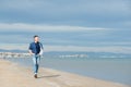 Handsome middle-aged man walking at the beach. Attractive happy smiling mid adult male model posing at seaside in blue jeans, t- Royalty Free Stock Photo