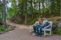 Handsome middle-aged man and young pretty lady sitting on bench and using smartphones in summer evening. Tourists on the beautiful Royalty Free Stock Photo