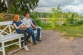 Handsome middle-aged man and young pretty lady sitting on bench and using smartphones in summer evening. Tourists on the beautiful Royalty Free Stock Photo