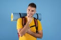 Handsome millennial guy with backpack and tourist mat smiling over blue background. Travel, tourism, camping, hiking