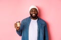 Handsome modern Black man drinking takeaway coffee, smiling and looking satisfied at camera, standing over pink