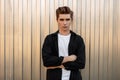 Handsome modern young man with a fashionable hairstyle in an elegant black shirt in a T-shirt poses near a silver wall in the city