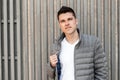 Handsome modern young man with a stylish hairstyle in a fashionable gray jacket in a trendy white T-shirt poses