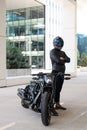 Handsome motorcyclist in helmet staying near his moto against urban backdrop