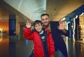 Handsome multi-ethnic man- dad and his son waving looking at camera while standing outside duty free shops in international Royalty Free Stock Photo