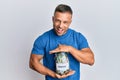 Handsome muscle man holding jar with savings smiling and laughing hard out loud because funny crazy joke